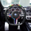 Front view of a BMW F chassis, M steering wheel in carbon fiber, extended paddle shifters, m color accents, black perforated leather, m color painted center trim, m color buttons, and led shift lights